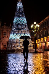Silhouette of a man with the umbrella looking at the Christmas tree in San Carlo Square, in the...