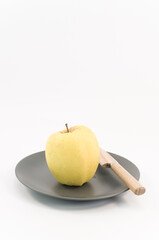 mela di colore giallo su piatto in ceramica grigia e coltello in legno su uno sfondo bianco, primo piano