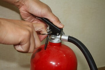 Hands pulling the safety pin from a red fire extinguisher. Preparing for use.