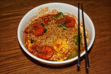 Close-up of a serving of Asian spicy noodles with shrimp and egg in a white bowl, ready to eat.