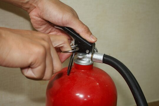 Hands pulling the safety pin from a red fire extinguisher. Preparing for use.