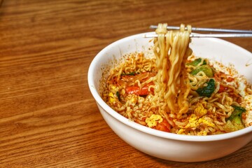 delicious instant noodles with shrimp, egg and vegetable toppings, in a white bowl on a wooden table
