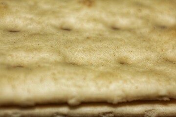 Close-up of the surface of a salted cracker biscuit with perforations and a slight break. Food texture.