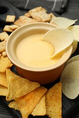 Tasty cheese dipping sauce in bowl and different snacks on table, closeup