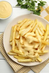 French fries with cheese sauce and parsley on white wooden table, flat lay