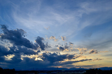 Dynamic Blue Sky with Swirling Gray Clouds and Yellow Hues Over a Distant Mountain Silhouette