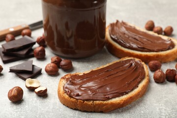Toasts with tasty hazelnut spread, chocolate pieces and nuts on grey table, closeup