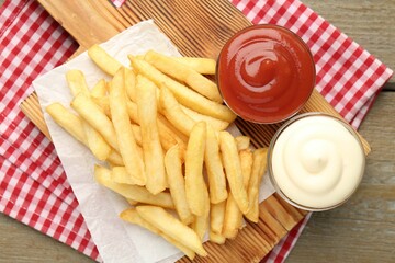 Tasty french fries with sauces on wooden table, top view