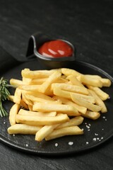 Tasty french fries served with ketchup and rosemary on black table, closeup
