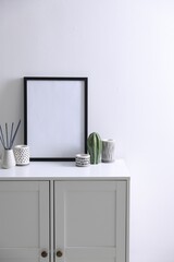 Empty picture frame, reed diffuser and stylish home decor on cabinet near white wall indoors