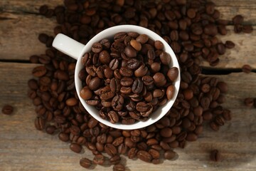 Aromatic coffee beans and cup on wooden table, flat lay
