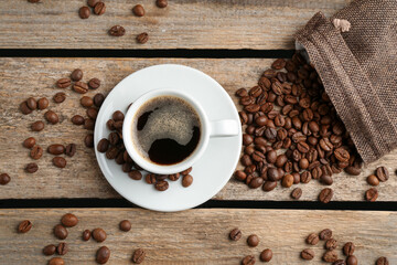 Aromatic coffee in cup and beans on wooden table, flat lay