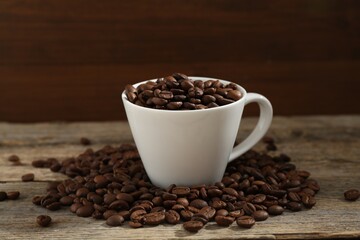 Aromatic coffee beans and cup on wooden table, closeup