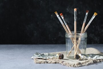 Brushes in jar and color paints on grey table. Space for text