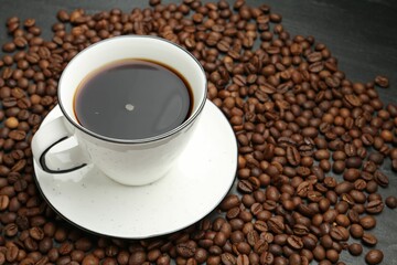 Aromatic coffee in cup and beans on black table, closeup. Space for text