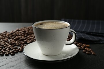 Aromatic coffee in cup and beans on black table, closeup