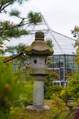 Serene view of an ancient stone lantern in a Japanese garden, contrasting with the modern architecture of a glass conservatory