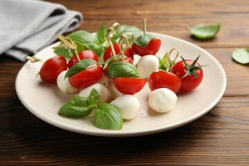 Appetizers with mozzarella, tomatoes and basil on wooden table, closeup
