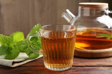 Aromatic lemon balm tea in glass cup, teapot and fresh leaves on wooden table