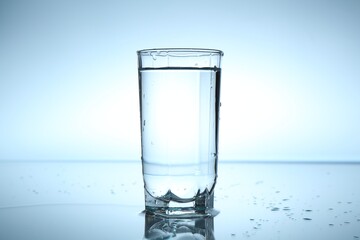 Fresh water in glass on mirror table against light blue gradient background, closeup