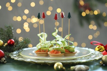 Tasty canapes and Christmas decor on green wooden table against background with blurred lights,...