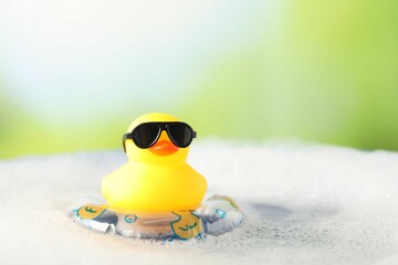 Obraz premium Cute rubber duck floating in water with bubbles against blurred green background, closeup