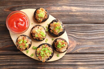 Delicious stuffed mushrooms and sauce on wooden table, top view. Space for text