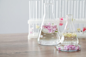Making luxury perfume. Essential oils in glassware and flowers on light wooden table, closeup. Space for text