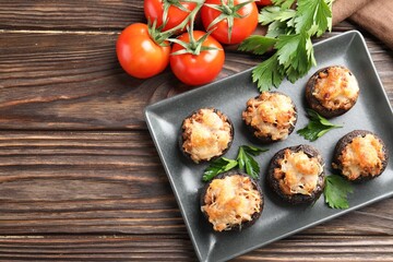 Delicious stuffed mushrooms with parsley and tomatoes on wooden table, flat lay. Space for text