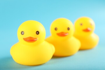 Three cute rubber ducks on light blue background, closeup