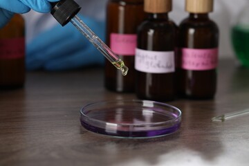 Professional perfumer developing luxury perfume at wooden table in laboratory, closeup