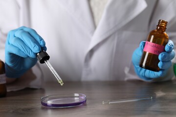Professional perfumer developing luxury perfume at wooden table in laboratory, closeup