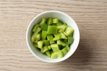 Pieces of fresh green bell pepper in bowl on wooden table, top view