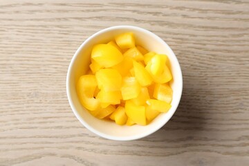 Pieces of fresh yellow bell pepper in bowl on wooden table, top view