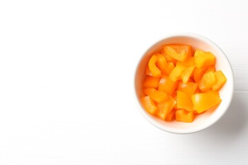 Pieces of fresh orange bell pepper in bowl on white wooden table, top view. Space for text