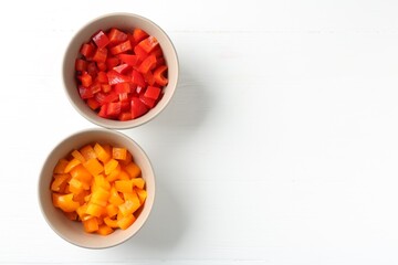 Pieces of fresh colorful bell peppers in bowls on white wooden table, flat lay. Space for text