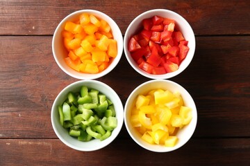 Pieces of fresh colorful bell peppers in bowls on wooden table, flat lay
