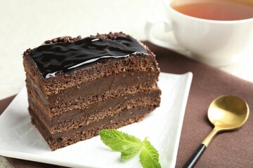 Piece of chocolate cake served with mint and spoon on table, closeup