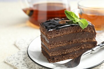 Piece of chocolate cake served with mint, fork and tea on white table, closeup. Space for text