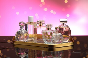 Many different perfume bottles on mirror surface against pink background with blurred lights,...