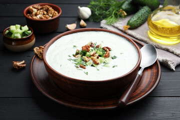 Tasty cucumber soup with dill and walnuts served on black wooden table, closeup
