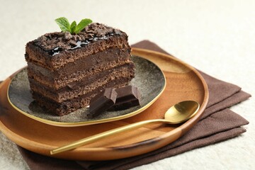 Piece of delicious chocolate cake with mint on white textured table, closeup