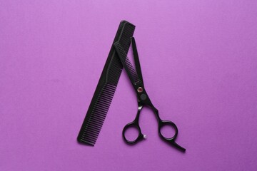 Scissors and comb on violet background, flat lay. Hairdresser's tools