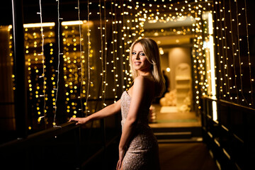 Elegant woman in sparkling dress poses among twinkling lights at a festive event