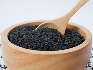 Wooden spoon scooping black sesame seeds from a natural wood bowl on a light background