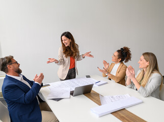 Cheerful business professionals with blueprints and laptop on table applauding for successful...