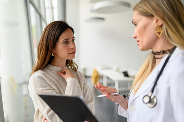 Female doctor with clipboard explaining diagnosis and treatment to worried young woman in hospital