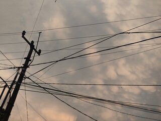 Silhouette of a utility pole with tangled wires against a cloudy evening sky. Represents urban...