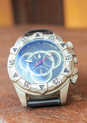 Luxury analog wristwatch with a black leather strap and stainless steel bezel, placed on a wooden...