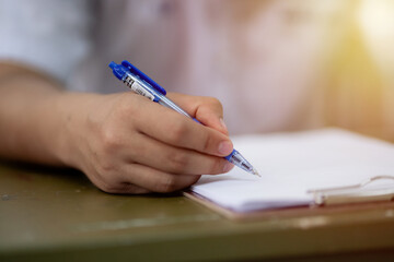 Close-up of hands holding a blue pen over a blank sheet on a clipboard, ready for writing, signing,...